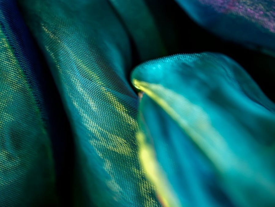 Close-up of iridescent turquoise fabric folds showing engineered pleat depth and grain